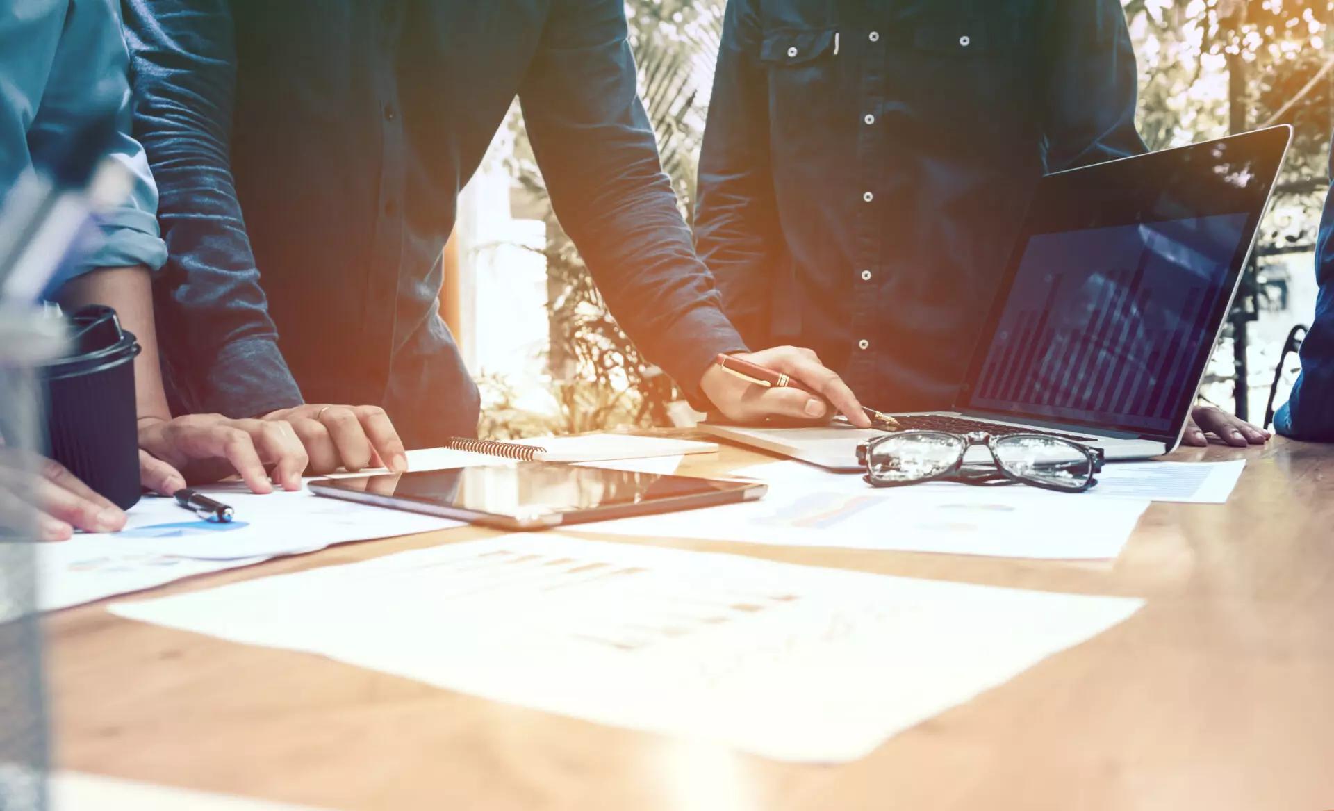 a table covered with business documents with people standing around it