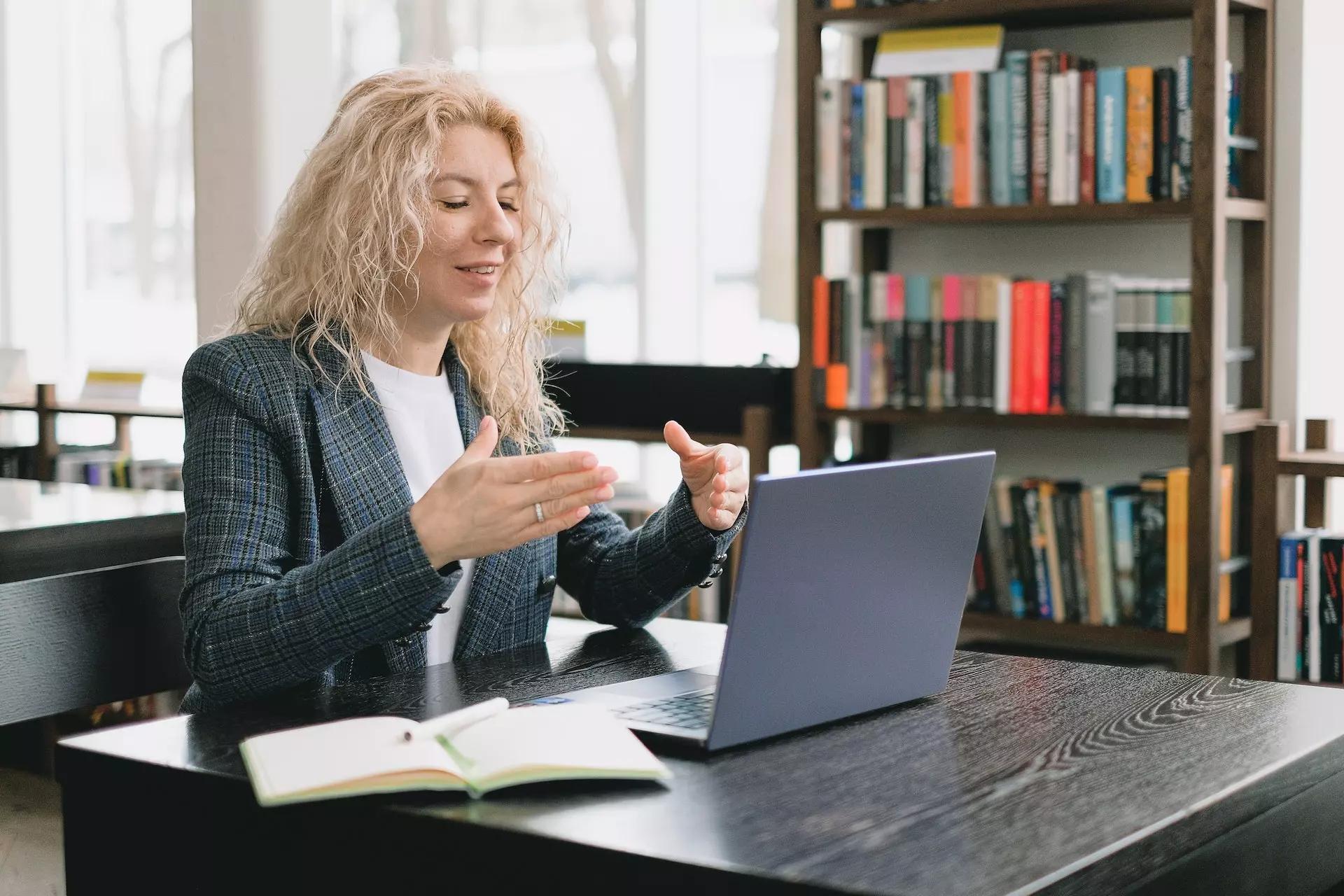 a person sitting in front of a laptop, gesturing as they speak towards the computer as on a video call