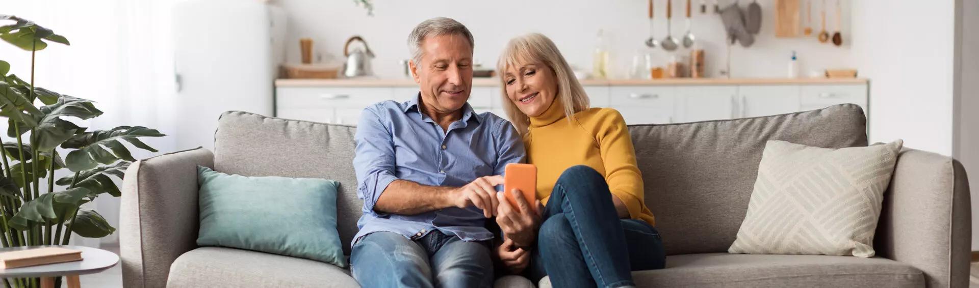 a couple sitting together on a couch and looking at a phone to view their charitable bunching strategy